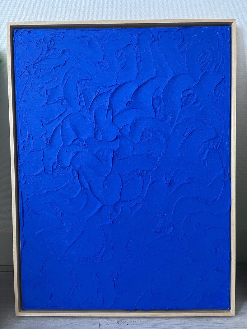 May include: A framed abstract painting with a textured blue surface. The painting is in a wooden frame.