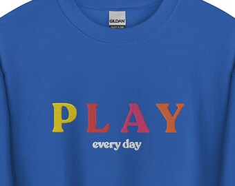 May include: A royal blue sweatshirt with the word "PLAY" embroidered in rainbow colors. The text "every day" is embroidered in white below the word "PLAY".
