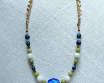 May include: A gold-tone chain necklace with colorful beaded accents. The necklace features a variety of beads in shades of blue, green, white, and gold, culminating in a large, vibrant blue central bead. The chain is adorned with small, colorful beads.