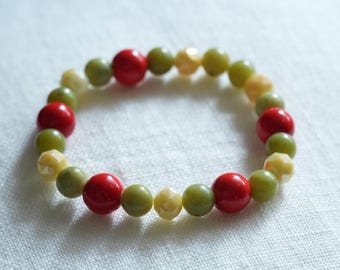 May include: A beaded bracelet featuring a mix of red, green, and yellow beads. The bracelet is made of round and faceted beads, strung together to form a circular shape. The beads are arranged in a repeating pattern.