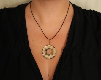 May include: A circular pendant featuring a faceted, iridescent surface with shades of green, gray, and brown. The pendant is suspended from a thin, dark brown cord necklace, creating a simple and clean design that rests against the chest area.