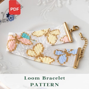 May include: A loom bracelet pattern PDF featuring a white background with a repeating design of small yellow, light blue, and pink butterflies made of tiny beads. The bracelet has gold-toned metal end bars and a gold-toned chain clasp closure.