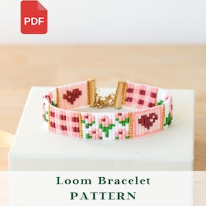 May include: A loom bracelet pattern featuring a pink, white, and green floral design with gold-colored clasps. The bracelet has a repeating pattern of hearts and flowers. The text "Loom Bracelet PATTERN" is displayed below the bracelet.