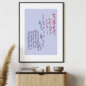 May include: A framed art print featuring abstract calligraphy in black and red ink on a light blue background. The artwork is displayed in a black frame and hangs on a white wall. The room is decorated with a vase of dried plants and a wooden cabinet.