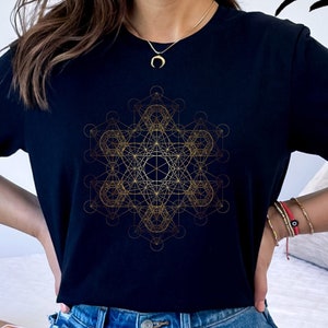 May include: Black t-shirt with a gold geometric design. The design is a complex pattern of lines and shapes, resembling a mandala or sacred geometry.