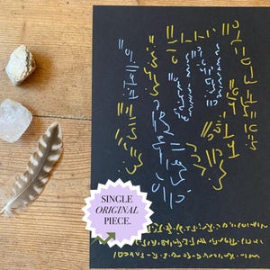 May include: A rectangular black paper sheet featuring hand-drawn gold and light blue abstract symbols and lines, accompanied by a brown and white striped feather, a clear quartz crystal, and a small white stone, with a sticker reading SINGLE ORIGINAL PIECE.