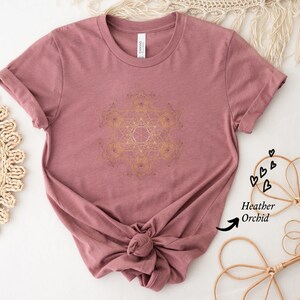 May include: A heather orchid t-shirt with a gold geometric design printed on the front. The shirt is made of a soft, comfortable fabric and has a relaxed fit.