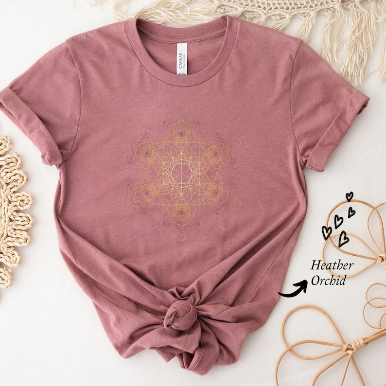 May include: A heather orchid t-shirt with a gold geometric design printed on the front. The shirt is made of a soft, comfortable fabric and has a relaxed fit.
