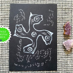 May include: A rectangular black card featuring a white hand-drawn illustration of a four-armed swirling symbol with circular centers, surrounded by intricate white script-like markings and a green starburst sticker labeled SINGLE ORIGINAL PIECE.