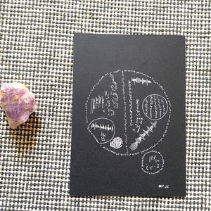 May include: A rectangular black card featuring a white circular design composed of abstract symbols, lines, and sound wave patterns, with the text #P.26 at the bottom right, accompanied by a small, rough-textured, light purple amethyst crystal cluster.