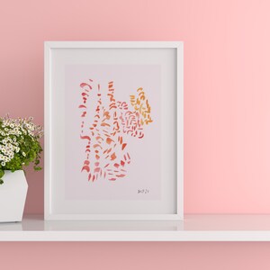 Puede incluir: Una impresión artística abstracta enmarcada con un borde blanco. La obra de arte presenta un diseño de acuarela en tonos naranja y rojo. A la izquierda del marco hay una maceta geométrica blanca con flores blancas. El fondo es rosa liso.