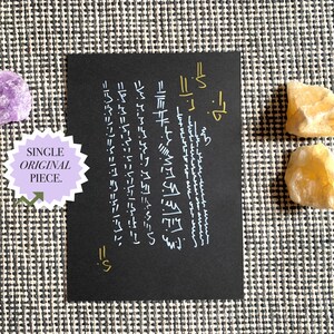 May include: A black card with white and gold script, accompanied by a purple and two yellow crystals. The card has the text "SINGLE ORIGINAL PIECE." The background is a black and white patterned fabric.