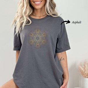 May include: A charcoal gray t-shirt with a gold geometric design. The design is a complex pattern of overlapping circles and lines. The shirt is made of a soft, comfortable fabric and has a relaxed fit.