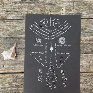 May include: A rectangular black card featuring white hand-drawn ink markings that resemble abstract symbols, spirals, and geometric patterns arranged in a symmetrical composition, accompanied by a small, light-colored seashell.