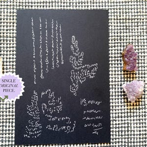 Könnte beinhalten: Eine rechteckige schwarze Karte mit weißer handschriftlicher Schrift und abstrakter Linienkunst, begleitet von einem klaren Quarzkristall und zwei kleinen violetten Amethystclustern. Ein hellvioletter sternförmiger Aufkleber trägt den Text SINGLE ORIGINAL PIECE.