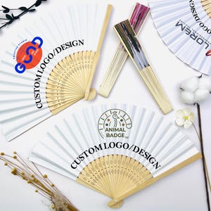 May include: Three white folding fans with bamboo ribs and custom printed logos. One fan features a blue and orange logo, another displays a black animal badge, and the third shows a colourful graphic. The fans are arranged with two open and one closed.