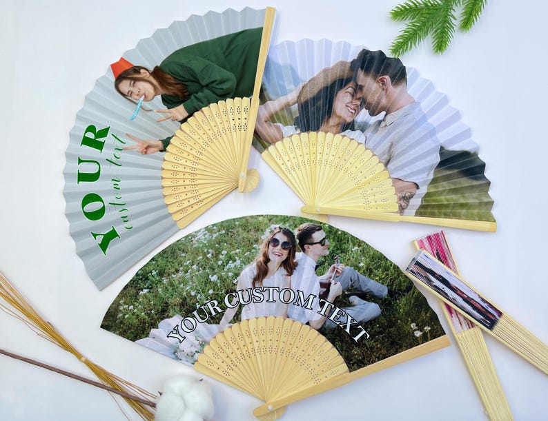 May include: Several open paper fans with wooden handles are displayed. The fans feature custom photos and text, including the words "YOUR custom text" and "YOUR CUSTOM TEXT". The fans have a light beige color and are decorated with images of people.