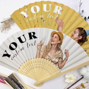 May include: Two personalized paper fans with the text "YOUR custom text". One fan is white with a photo of a woman holding a champagne glass. The other fan is yellow with confetti.