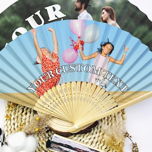 May include: A custom-printed hand fan with a light blue background and the text "YOUR CUSTOM TEXT". The fan features images of people and children holding balloons. The fan is made of wood and paper.