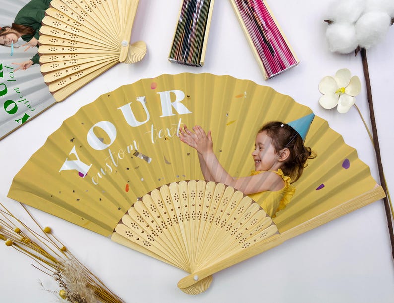 May include: Yellow folding fan with a photo of a child wearing a party hat. The fan has the text "YOUR custom text" in white. The fan is made of wood and paper. Other fans are visible in the background.