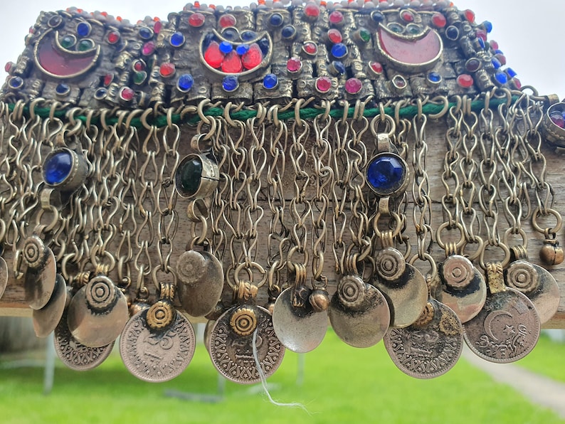 May include: A silver and gold necklace with a chain fringe and coin-like charms. The necklace is decorated with red, blue, and green gemstones.