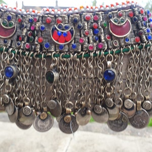 May include: A silver necklace with a row of colorful beads and metal charms. The necklace has a fringe of silver chains and coins.