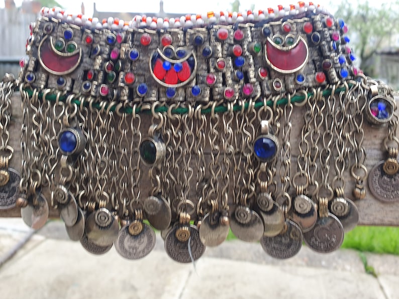 May include: A silver necklace with a row of colorful beads and metal charms. The necklace has a fringe of silver chains and coins.