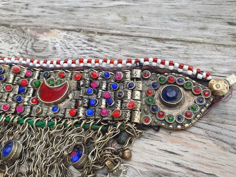 May include: A silver and gold colored necklace with red, blue, and green glass beads. The necklace has a fringe of silver chains and beads.