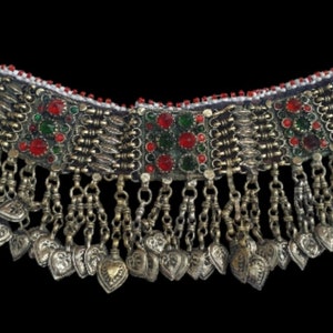 May include: A silver and gold necklace with red and green glass beads and a fringe of silver charms. The necklace is made of metal and has a traditional design.