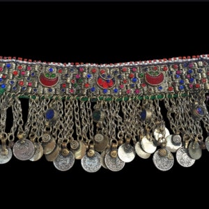 May include: A silver and gold necklace with a beaded band and a fringe of silver coins. The band is decorated with red, blue, and green stones.