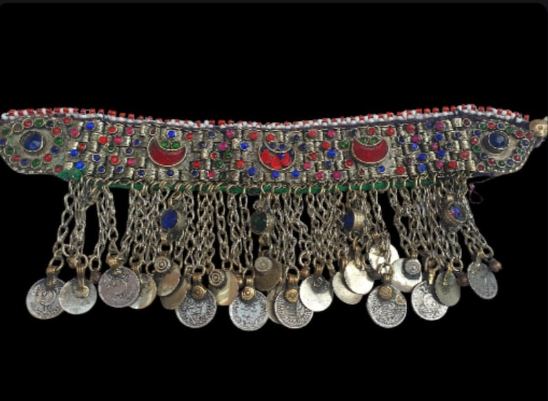 May include: A silver and gold necklace with a beaded band and a fringe of silver coins. The band is decorated with red, blue, and green stones.