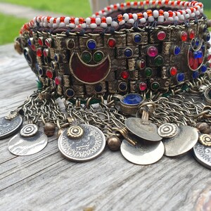 May include: A silver and gold necklace with red, blue, and green glass beads, and silver coins hanging from the bottom.