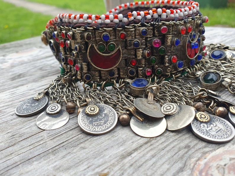 May include: A silver and gold necklace with red, blue, and green glass beads, and silver coins hanging from the bottom.