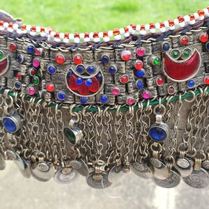 May include: A silver necklace with red, blue, and green glass beads and silver coin charms. The necklace has a fringe of silver chains and beads.