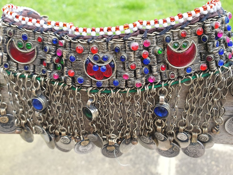 May include: A silver necklace with red, blue, and green glass beads and silver coin charms. The necklace has a fringe of silver chains and beads.