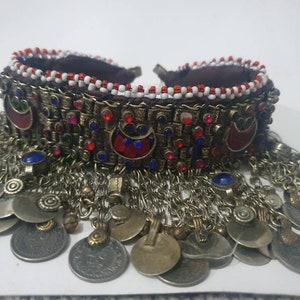 May include: A silver and gold necklace with red, blue, and green beads and a fringe of silver coins. The necklace is made of metal and has a beaded band with a decorative design.
