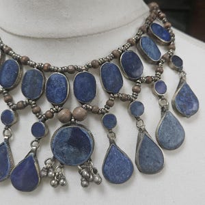 May include: A silver and blue necklace with multiple strands of beads and large, teardrop-shaped lapis lazuli stones.