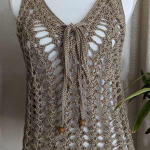 May include: A crocheted tank top with a brown color and a tie at the neck. The top has a delicate openwork pattern and wooden beads on the ties.