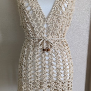Peut inclure: Une robe en crochet beige avec un décolleté en V et une ceinture à nouer à la taille. La robe a un motif délicat en tissage ouvert et est parfaite pour une journée d'été.