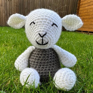 May include: A white crocheted lamb with a gray crocheted body. The lamb has a smiling face with black eyes and a black nose.