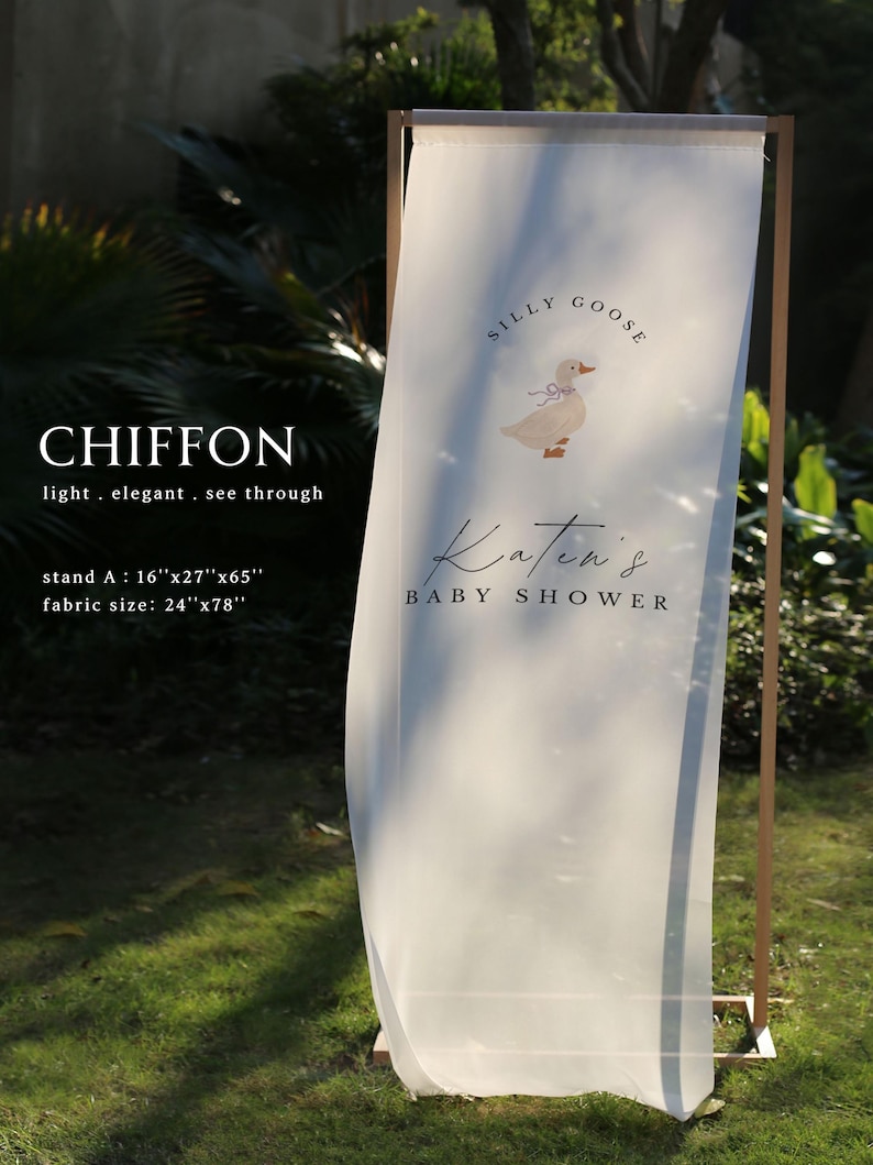 May include: A sheer white chiffon fabric banner hanging on a wooden frame. The banner features a graphic of a goose with a blue bow and the text "SILLY GOOSE" and "Katen's BABY SHOWER". The stand measures 16"x27"x65" and the fabric is 24"x78".