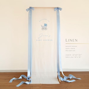 May include: A baby shower welcome sign with a light blue stroller illustration and the text "Welcome to Jean's Baby Shower." The sign is made of linen and has light blue ribbons. Stand B: 22"x27"x67", fabric size: 24"x 78".