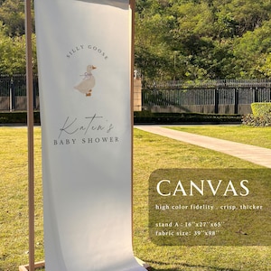 May include: A vertical off-white fabric banner on a wooden frame featuring a graphic of a goose with a blue bow and the text "Silly Goose Katen's Baby Shower". The banner includes text stating "CANVAS high color fidelity . crisp. thicker" with dimensions "stand A : 16"x27"x65"" and "fabric size: 39"x98"".
