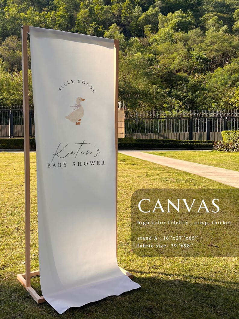 May include: A vertical off-white fabric banner on a wooden frame featuring a graphic of a goose with a blue bow and the text "Silly Goose Katen's Baby Shower". The banner includes text stating "CANVAS high color fidelity . crisp. thicker" with dimensions "stand A : 16"x27"x65"" and "fabric size: 39"x98"".