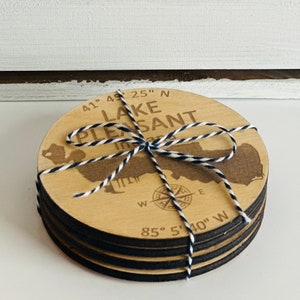 May include: Set of four wooden coasters featuring a map of Lake Pleasant, Michigan. The coasters are tied together with twine and have a compass rose design. The coordinates 41° 45' 25" N and 85° 5' 40" W are printed on the coasters.