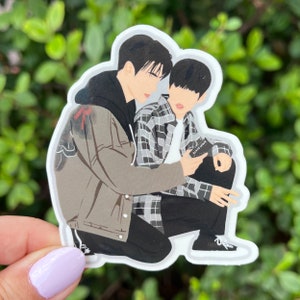 Puede incluir: Dos figuras de dibujos animados, una con una chaqueta marrón y la otra con una camisa a cuadros, están arrodillados y mirando un pequeño objeto negro con el texto "BLACK ROSE" en él.