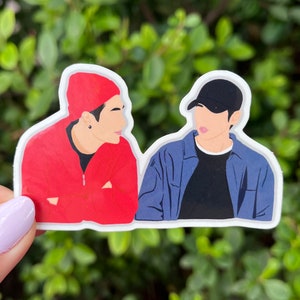 Puede incluir: Dos figuras de dibujos animados, una con una sudadera roja y una boina roja, la otra con una chaqueta azul y una gorra de béisbol negra, se miran.