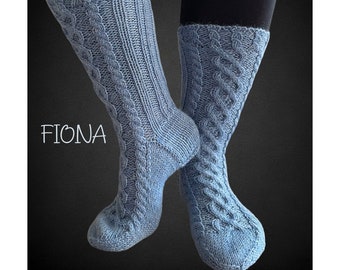Peut inclure: Une paire de chaussettes bleues en tricot avec un motif en câble. Les chaussettes sont présentées sur les jambes d'une personne. Le mot "FIONA" est écrit en blanc sur le côté gauche de l'image.