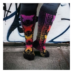 May include: A pair of knee-high socks with a vibrant gradient pattern. The socks transition from black at the top and foot to a mix of yellow, orange, and pink in the center. The design features geometric and floral motifs.