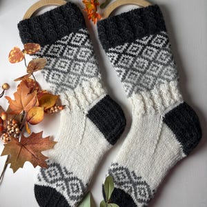 May include: A pair of knitted socks with a black, white, and gray geometric pattern. The socks are made with a soft, warm yarn and are perfect for keeping your feet cozy in the winter.